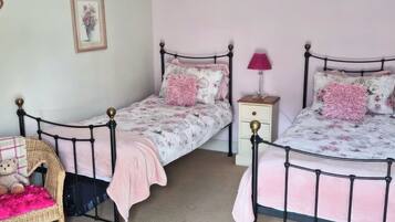 A bedroom with two twin beds, a nightstand, a lamp, a wicker chair, and a teddy bear.