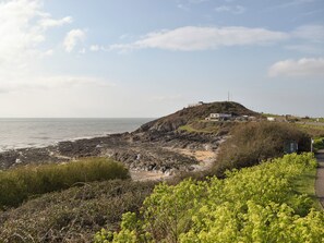 A coastal landscape with a hill featuring a building, rocky shoreline, and greenery. - 2 bedroom accommodation in Three Crosses, Gower, Swansea (Three Crosses, Gower, Swansea)