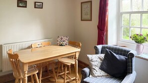 Un área de comedor con una mesa y sillas de madera, un sofá de estampado cuadriculado, un radiador y una ventana con cortinas.