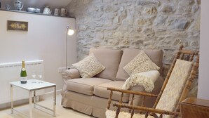 Una sala de estar acogedora con una pared de piedra, un sofá color beige, una silla de madera, una mesita con una botella de cava y dos copas.