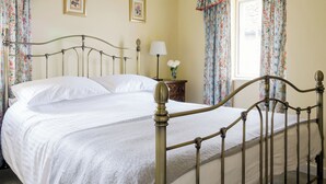 Un lit avec un cadre en métal, deux tables de chevet, une lampe et des rideaux à motifs floraux.