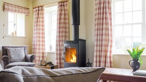 A cozy living room with a fireplace, plaid curtains, a sofa, and a window with a view.