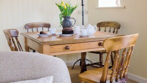 Une table à manger avec des chaises, un vase rempli de fleurs, un pichet, une théière, des tasses et un gâteau.