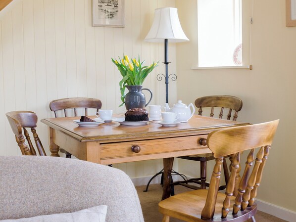 A dining table with chairs, a vase with flowers, a pitcher, a teapot, cups, and a cake.