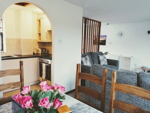 A living room with a sofa, a table with a vase of flowers, and a kitchen area with a toaster.