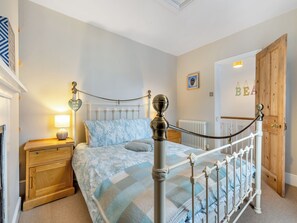 Un dormitorio con una cama, mesitas de noche de madera, un radiador y una puerta con marco de madera.
