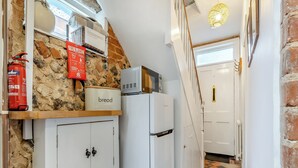 A narrow hallway with a stone wall, a fire blanket, a bread container, and a white refrigerator. - 3 bedroom accommodation in Cromer (Cromer)