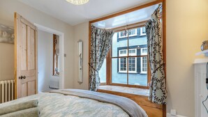 A bedroom with a large bed, a window with curtains, a radiator, and a wooden door. - 3 bedroom accommodation in Cromer (Cromer)
