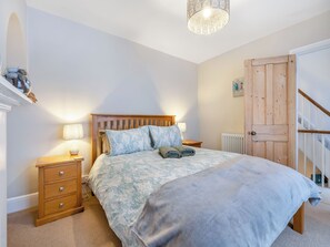 A bedroom with a wooden bed, bedside tables, a radiator, and a staircase.