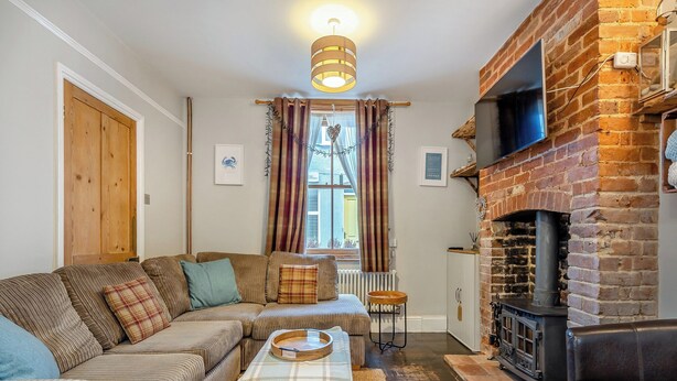 A cozy living room with a sectional sofa, a fireplace, and a large window with curtains. - 3 bedroom accommodation in Cromer (Cromer)