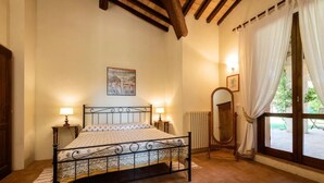 A bedroom with a metal bed frame, two bedside lamps, a poster on the wall, a mirror, and a window with curtains. - Bacco (Montefalco)