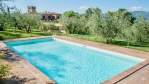 A rectangular swimming pool with clear blue water, surrounded by a brick deck and lush greenery. - Bacco (Montefalco)
