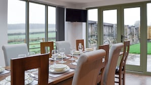 Un coin repas avec une table dressée pour quatre personnes, de grandes fenêtres et un téléviseur à écran plat fixé au mur.