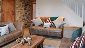 Un salon chaleureux avec un mur en pierre, un plafond en bois et un escalier.