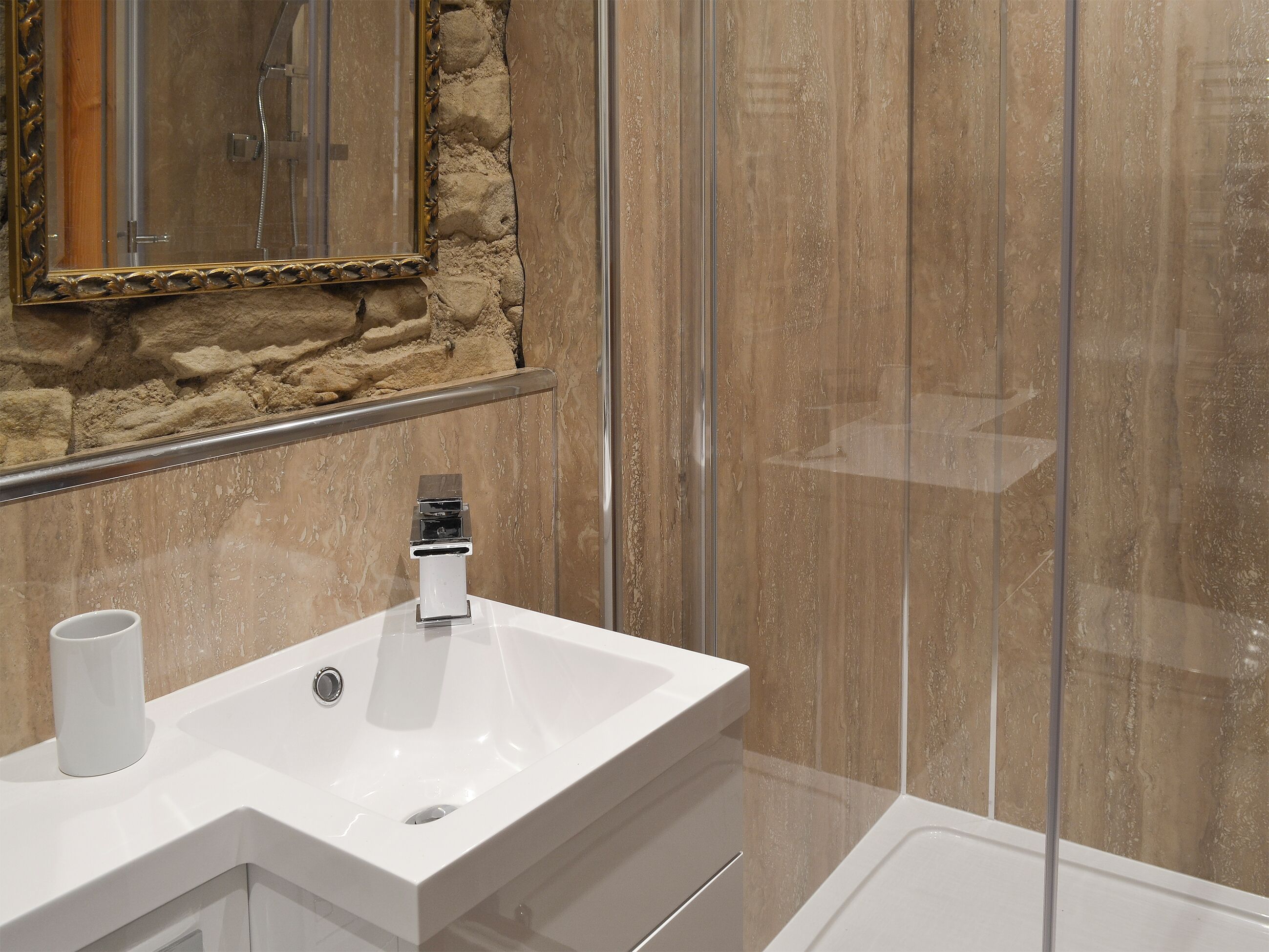 A bathroom with a white sink, a mirror with an ornate frame, and a shower area with a stone wall backdrop.