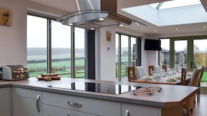 Une cuisine moderne dotée d’un grand îlot central, d’un four encastré et offrant une vue sur la campagne.