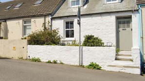 A two-story white house with a grey roof, a front door, and a small garden area.
