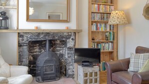A living room with a stone fireplace, a television on a wooden stand, a bookshelf, and a leather sofa.
