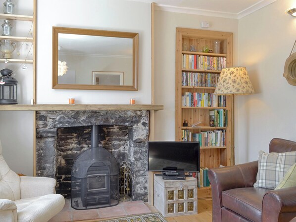 A living room with a stone fireplace, a television on a wooden stand, a bookshelf, and a leather sofa.