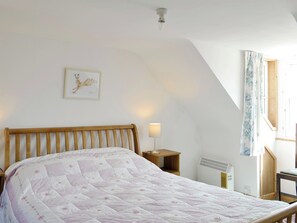 Un dormitorio con una cama de madera, una mesita de noche con lámpara, un radiador y una ventana con cortinas.