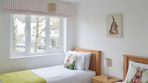 A bedroom with two single beds, a window with a view of the street, and a painting on the wall. - 2 bedroom accommodation in Bowness-on-Windermere (Bowness-on-Windermere)