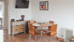 A modern dining area with a round table and four chairs, a television mounted on the wall, and a framed artwork above the table. - 2 bedroom accommodation in Bowness-on-Windermere (Bowness-on-Windermere)