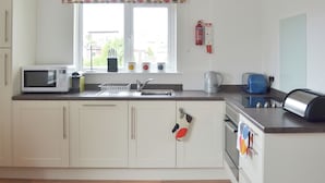 A modern kitchen with white cabinets, a microwave, a kettle, a toaster, and a sink. - 2 bedroom accommodation in Bowness-on-Windermere (Bowness-on-Windermere)