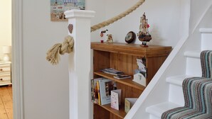 A staircase with a wooden shelf holding books, a ship model, and a dog figurine.