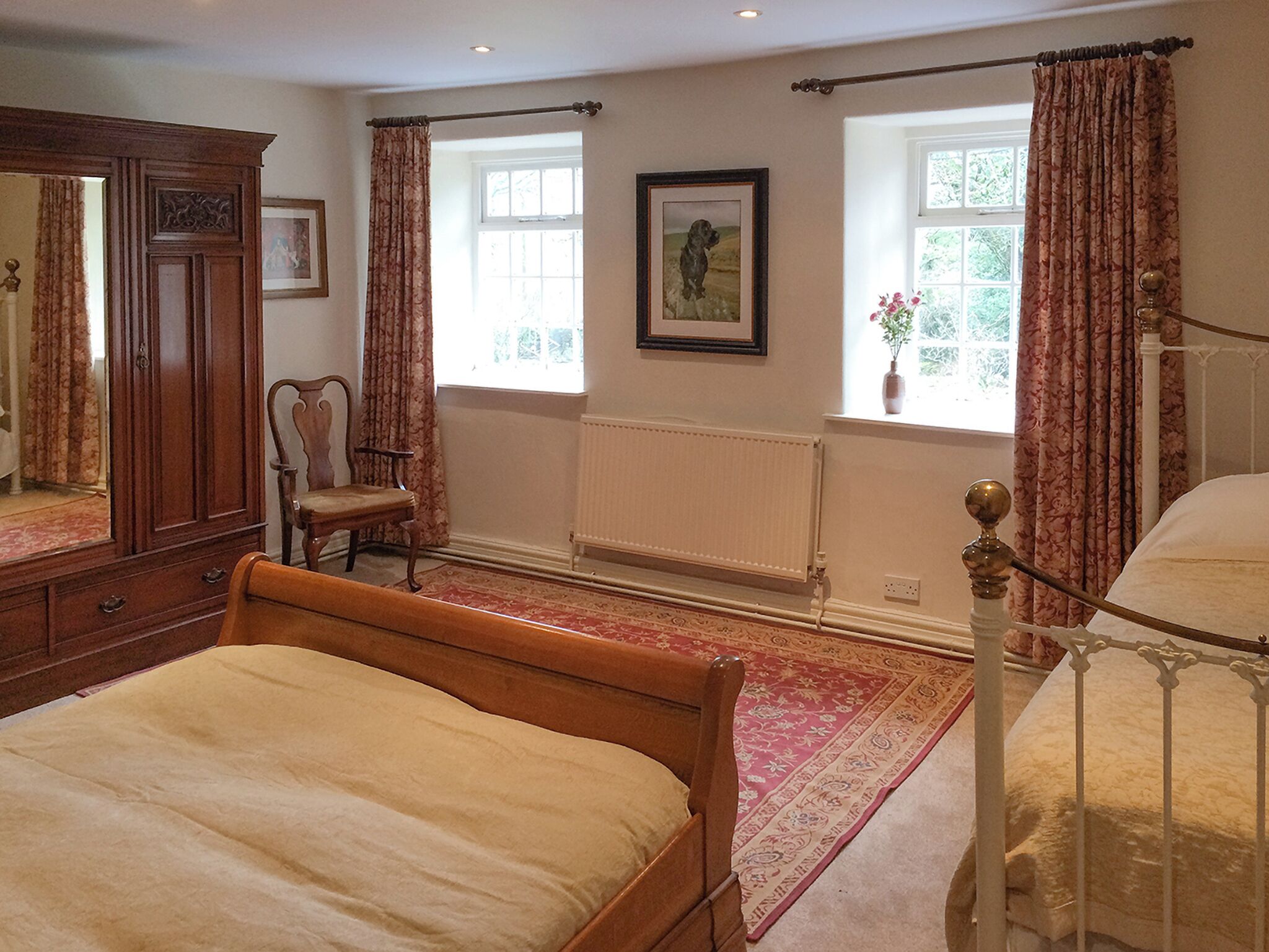A bedroom with a wooden bed, a chair, a wardrobe, and a window with curtains.