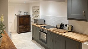 Una cocina con gabinetes grises, encimera de madera, microondas, tostadora y hervidor.
