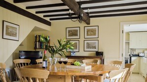 A dining room with a wooden table and chairs, a wine bottle, glasses, and a fruit platter. - Hungate Garden Cottage (Pickering)
