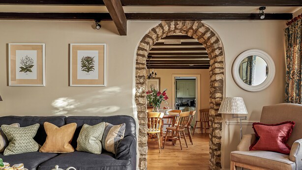 A cozy living room with a sofa, a dining table, and a kitchen in the background. - Hungate Garden Cottage (Pickering)