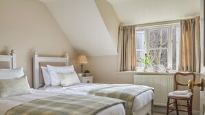A bedroom with two beds, a window with curtains, a radiator, and a chair. - Hungate Garden Cottage (Pickering)
