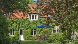 A garden with a lawn, a wooden table and chairs, and a blue umbrella. - Hungate Garden Cottage (Pickering)