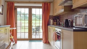 Eine Küche mit Holzausstattung, einer Mikrowelle und Blick auf einen Garten durch Glastüren.