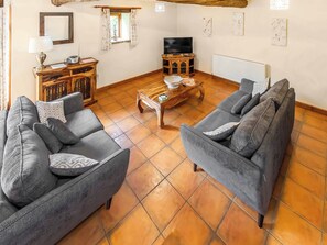 Un salon avec deux canapés gris, une table basse en bois, un téléviseur et une fenêtre avec des rideaux.
