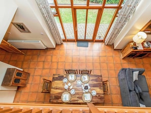 A dining area with a wooden table set for four, a sofa, and a view of a garden through large windows. - 2 bedroom accommodation in Catfield (Catfield)