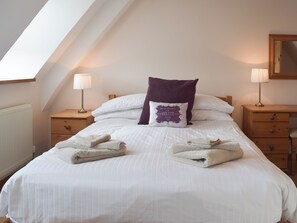 A neatly made bed with white linens and a purple pillow, two bedside tables with lamps, and a wooden nightstand. - 2 bedroom accommodation in Catfield (Catfield)