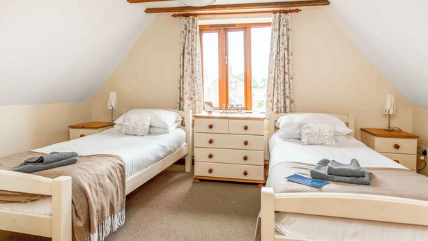 A bedroom with two single beds, a dresser, a nightstand, and a window with curtains. - 2 bedroom accommodation in Catfield (Catfield)