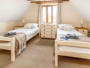 Een slaapkamer met twee eenpersoonsbedden, een dressoir, een nachtkastje en een raam met gordijnen.