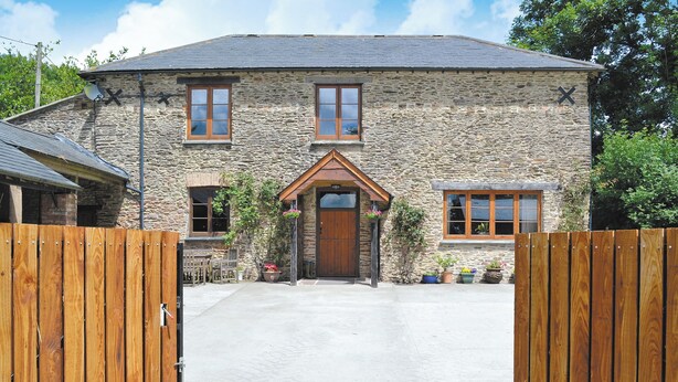 A stone building with a wooden door and windows, a paved driveway, and a wooden fence. - The Coach House - EXG (Upton, near Dulverton)