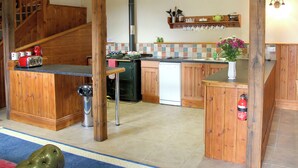 A kitchen with wooden cabinets, a dishwasher, a stove, and a sink. There is a wooden staircase leading to another level. - The Coach House - EXG (Upton, near Dulverton)