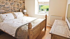Un dormitorio con pared de piedra, cama de madera, ventana con vistas a la vegetación y un radiador.