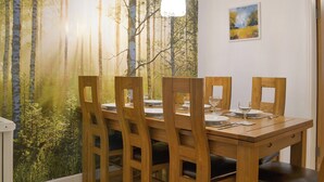 Ruokailutilassa on puinen pöytä ja tuolit, seinällä on metsäaiheinen seinämaalaus, katosta roikkuu valaisin ja seinällä on pieni taulu.
