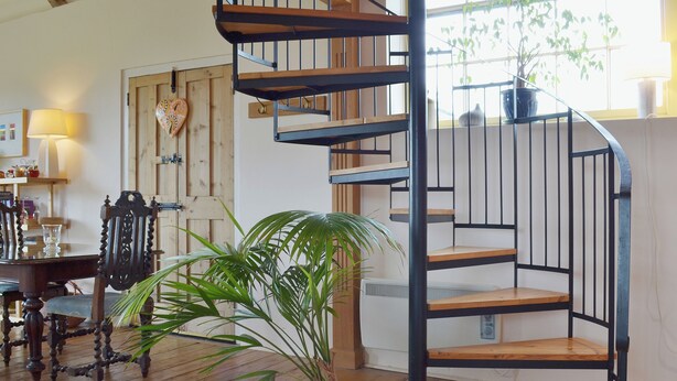 A spiral staircase with wooden steps and metal railings, a potted plant, and a wooden floor. - 1 bedroom accommodation in Burcott, Wells (Burcott, Wells)