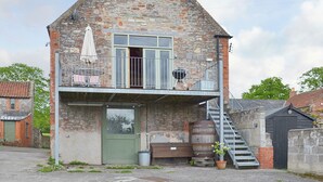A stone building with a balcony, a door, and a staircase leading to an upper level. - 1 bedroom accommodation in Burcott, Wells (Burcott, Wells)