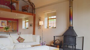 A spacious living room with a white sofa, a wooden table, a black fireplace, and a balcony. - 1 bedroom accommodation in Burcott, Wells (Burcott, Wells)