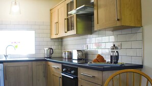 A kitchen with wooden cabinets, a stove, a sink, and a dining area with a chair and a table. - 2 bedroom accommodation in Bassenthwaite, near Keswick (Bassenthwaite, near Keswick)