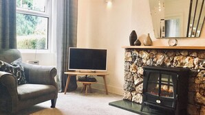 A living room with a sofa, a flat-screen TV, a stone fireplace, and a window with curtains. - 2 bedroom accommodation in Bassenthwaite, near Keswick (Bassenthwaite, near Keswick)