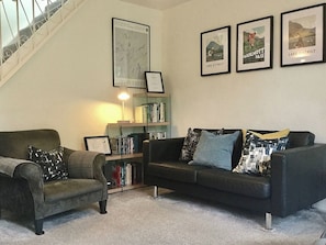 A living room with a staircase, a bookshelf, and three framed pictures on the wall.